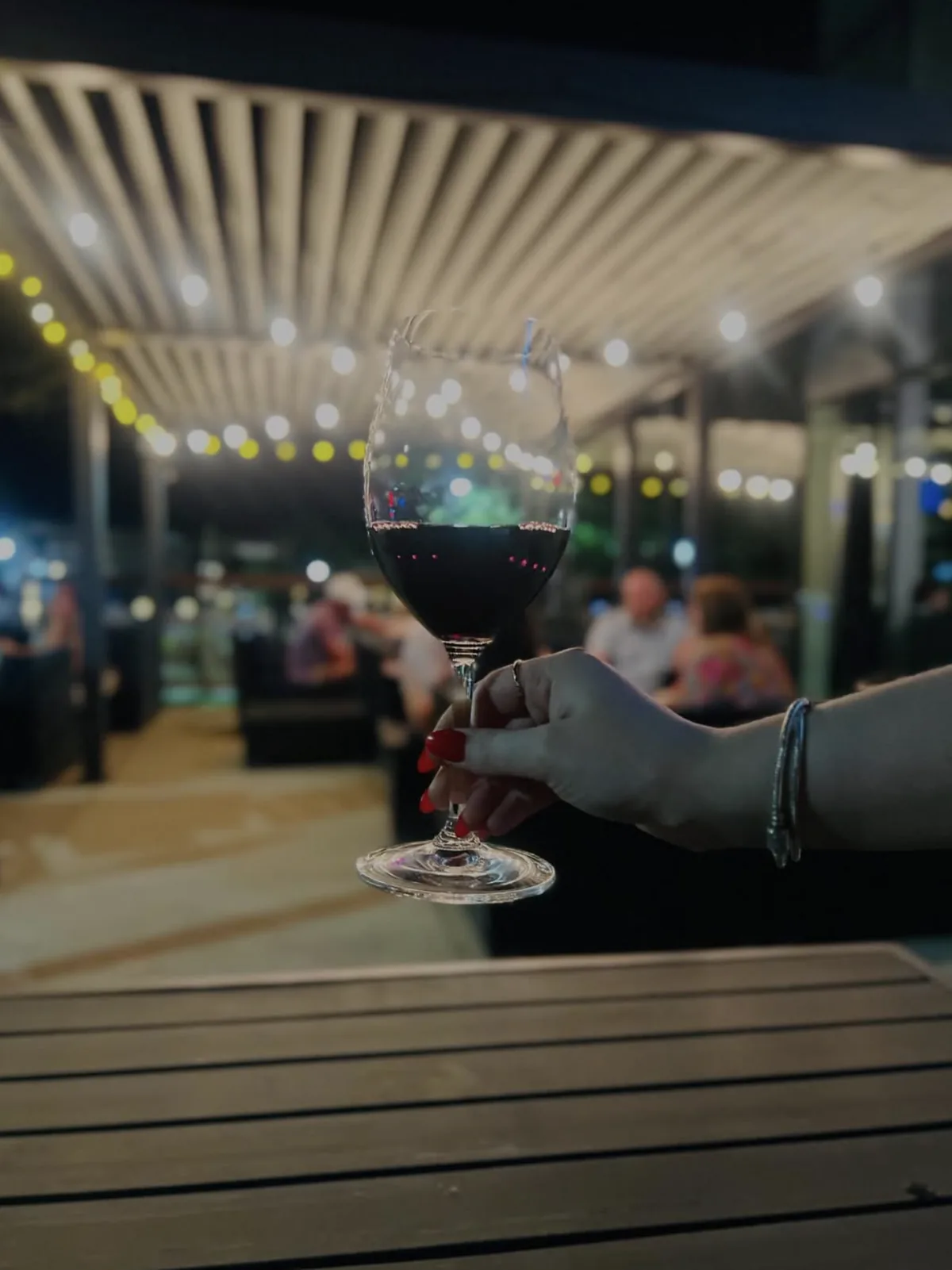 Hand holding a glass of red wine at an outdoor patio event