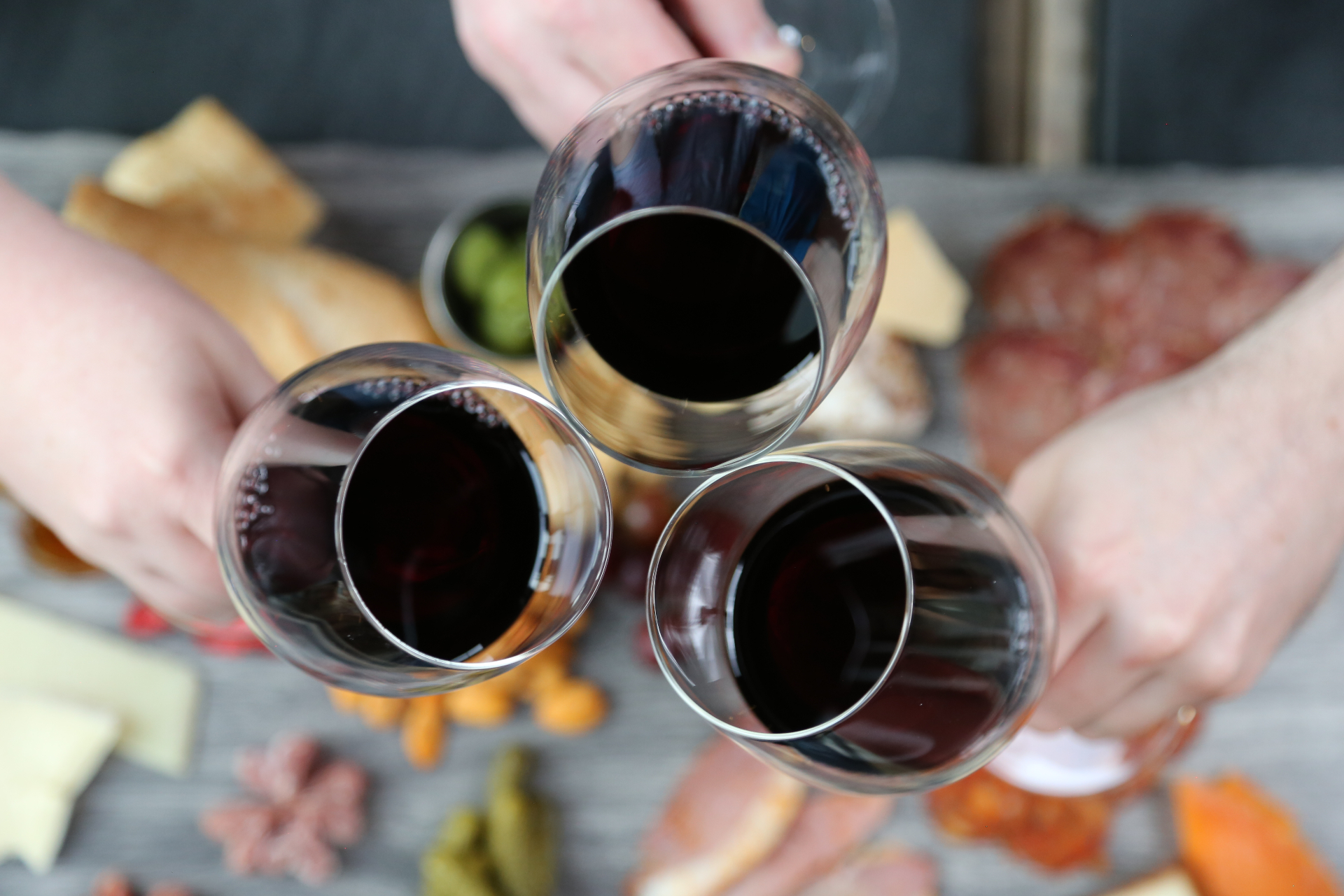 Three wine glasses toasting over a charcuterie board
